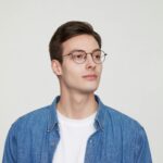 Portrait of a stylish young man in glasses wearing a denim shirt.